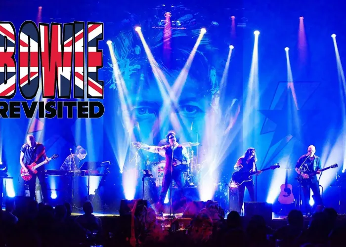 Six band members on stage,  dramatic stage lighting, David Bowie's face in background