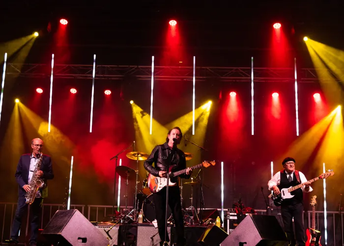 Three band members on stage with red and yellow lights in background
