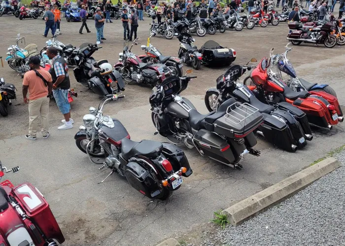 Many motorcycles lined up in rows in parking lot, tent pop ups in background