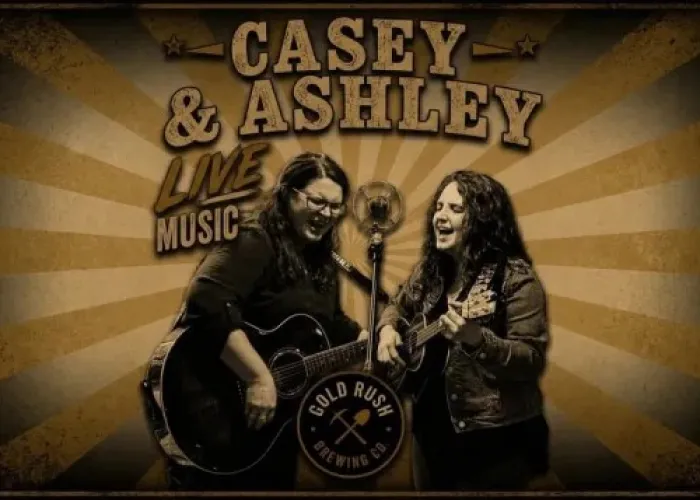 Casey and Ashley in black and white singing into a microphone together, both holding guitars, name of event