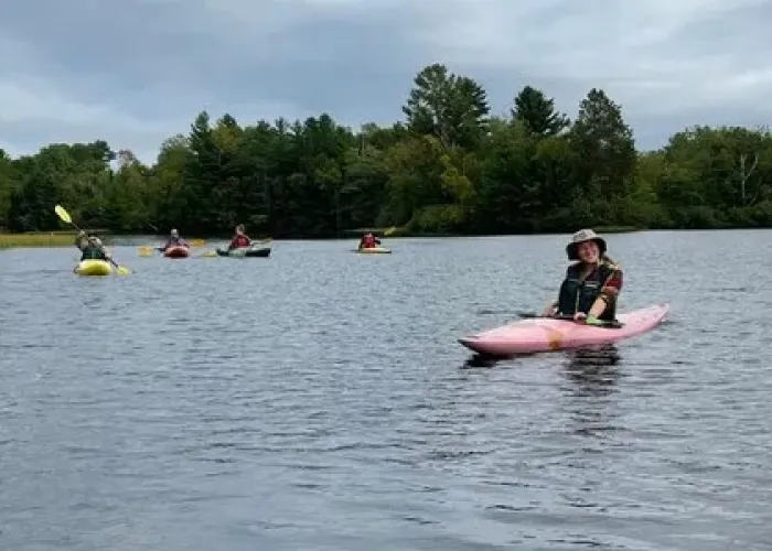 Several Kayakers on lake, trees in background, cloudy sky