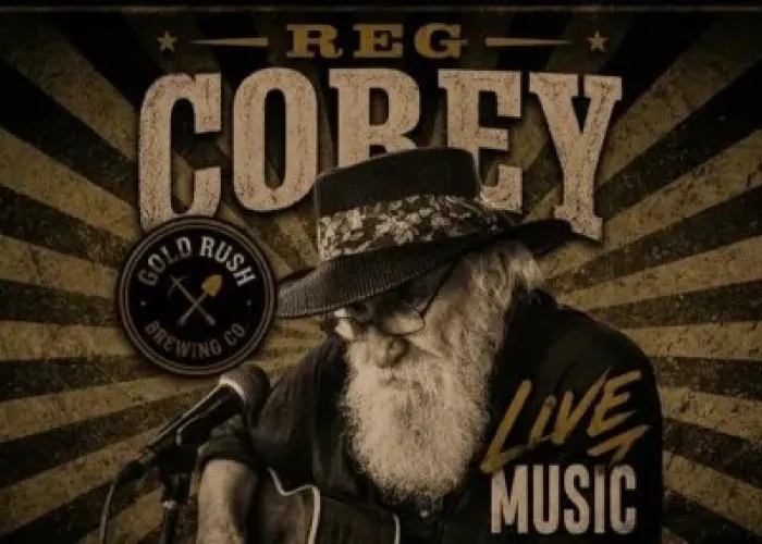 Black and white photo of Reg Corey holding guitar in front of microphone, sitting down. Black and beige striped background