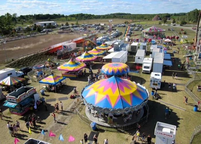 Multiple colourful tents, trailers, people participating in fair events, rides, cars